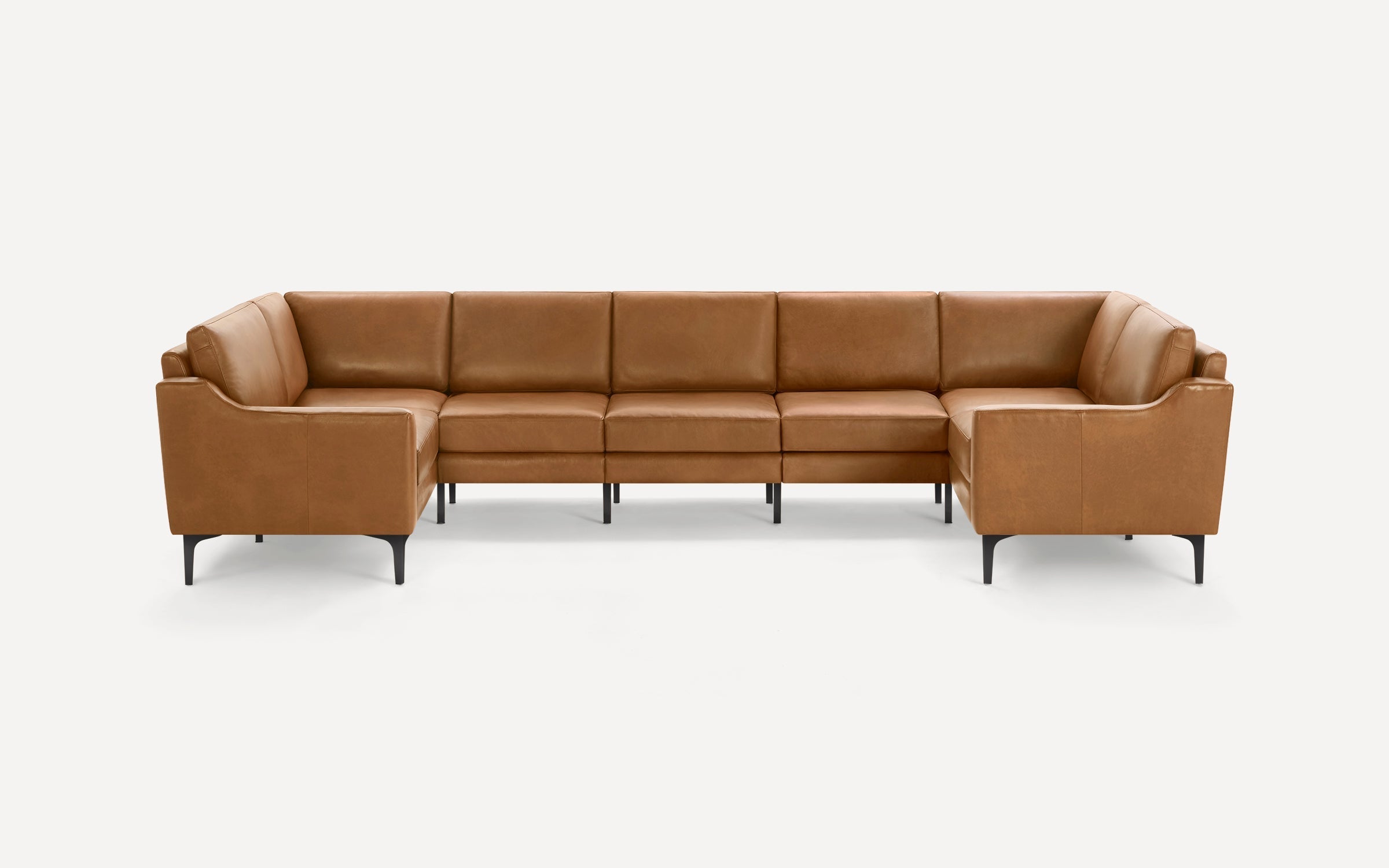 Large modern U-shaped sectional sofa with smooth tan leather upholstery and slim black metal legs on white background.