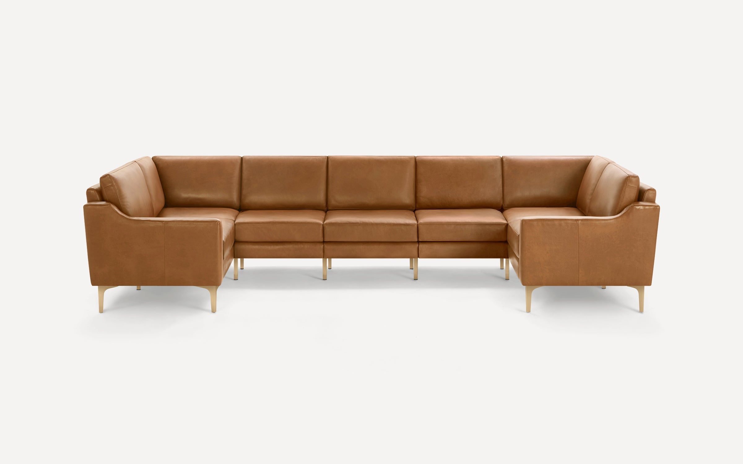 Large L-shaped sectional sofa with tan leather upholstery and slender light wooden legs against plain white background.