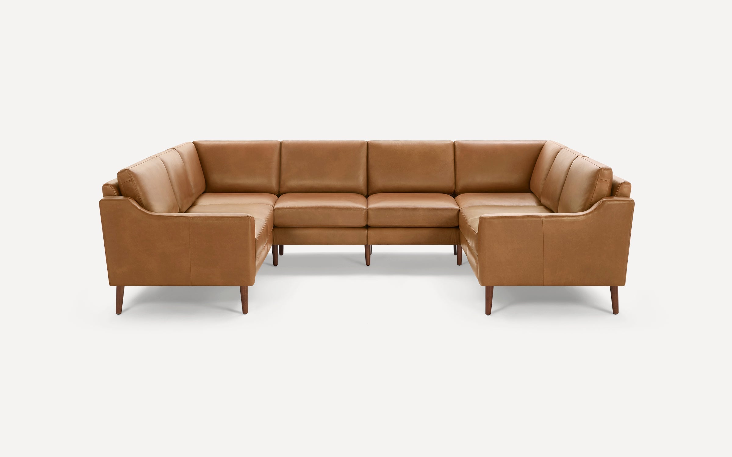 Tan leather U-shaped sectional sofa with clean lines, cushioned seats, and wooden tapered legs on white background.