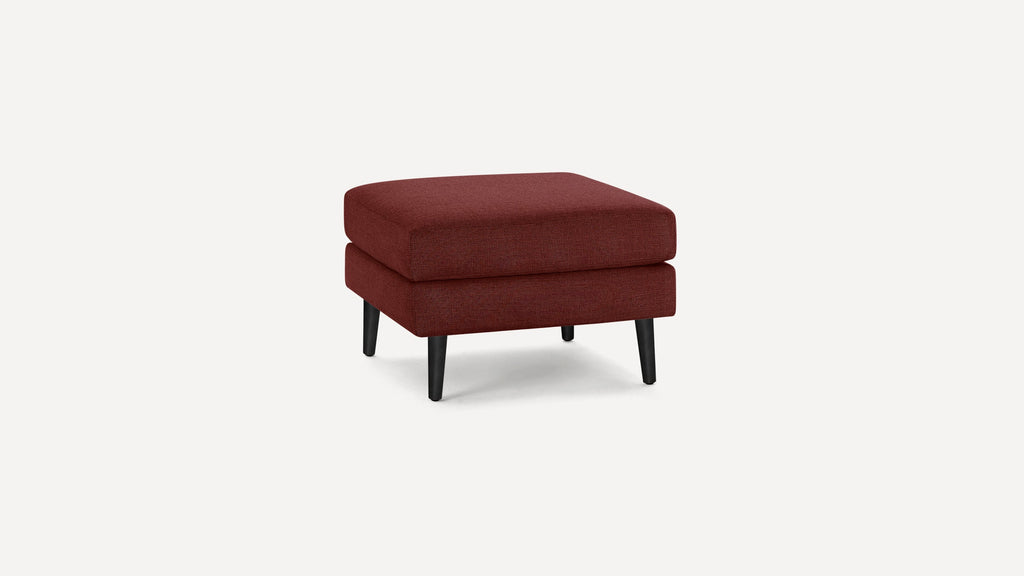 Square, modern ottoman upholstered in deep red fabric with four black tapered wooden legs on a plain white background.