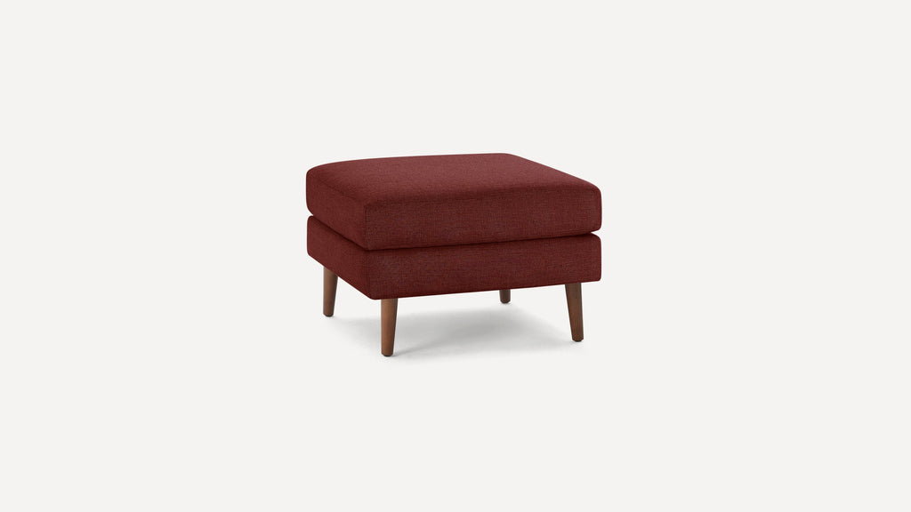 Square, mid-century modern ottoman with burgundy fabric upholstery and wooden tapered legs on a white background.