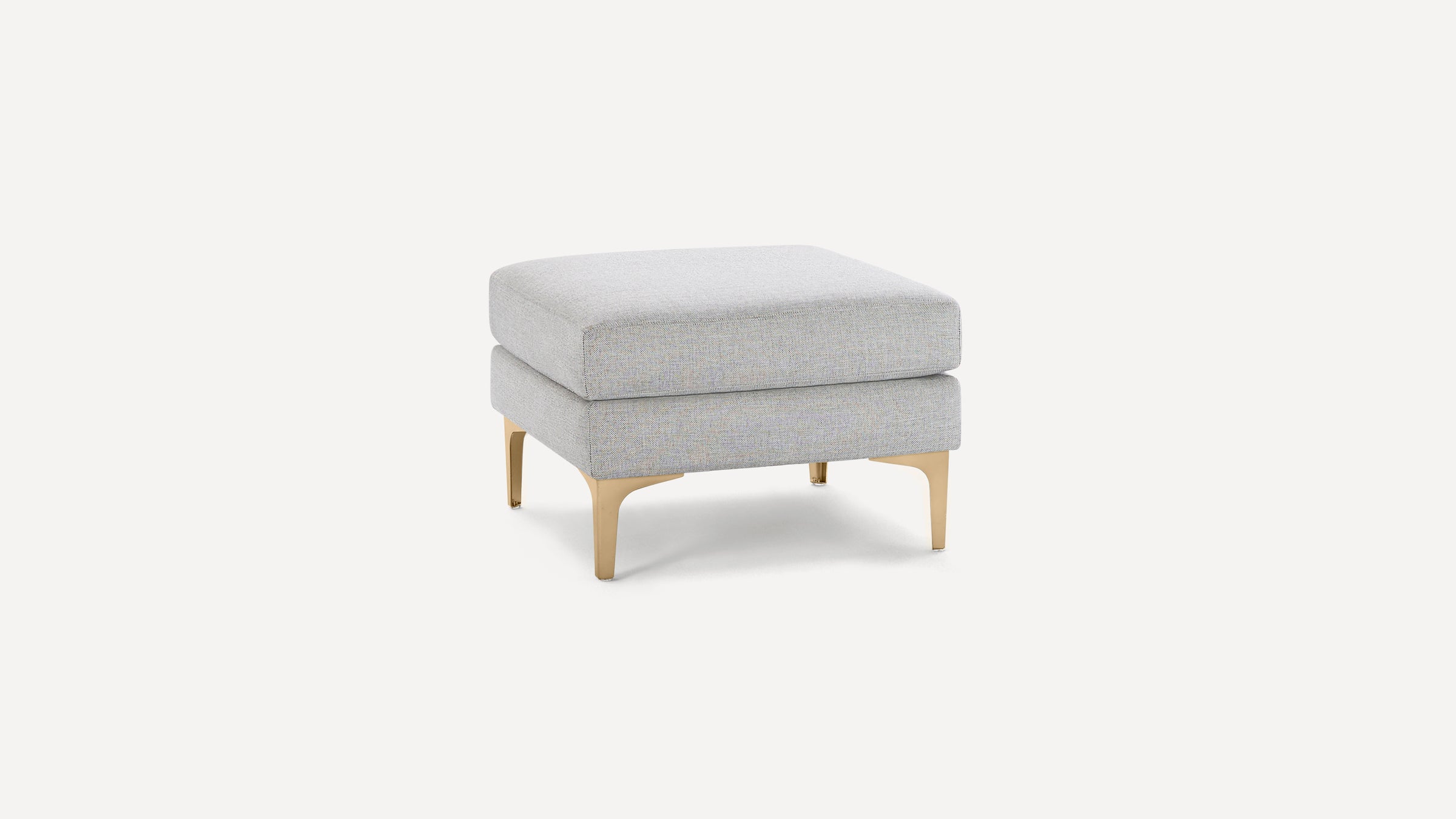 Square light grey upholstered ottoman with cushioned top and gold-colored metal legs on a white background.