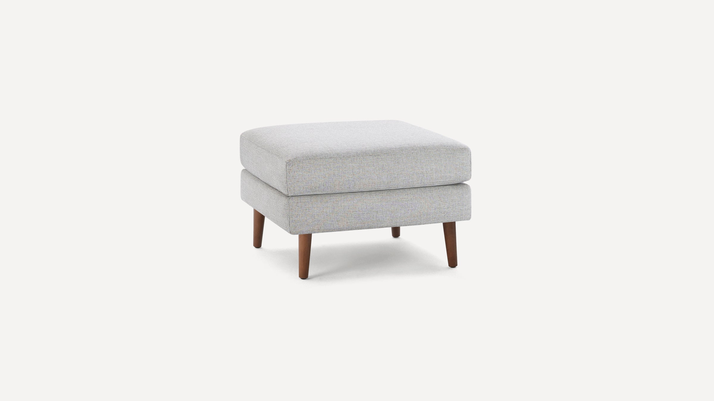 Modern square ottoman with light gray fabric upholstery and tapered wooden legs, minimalist design.