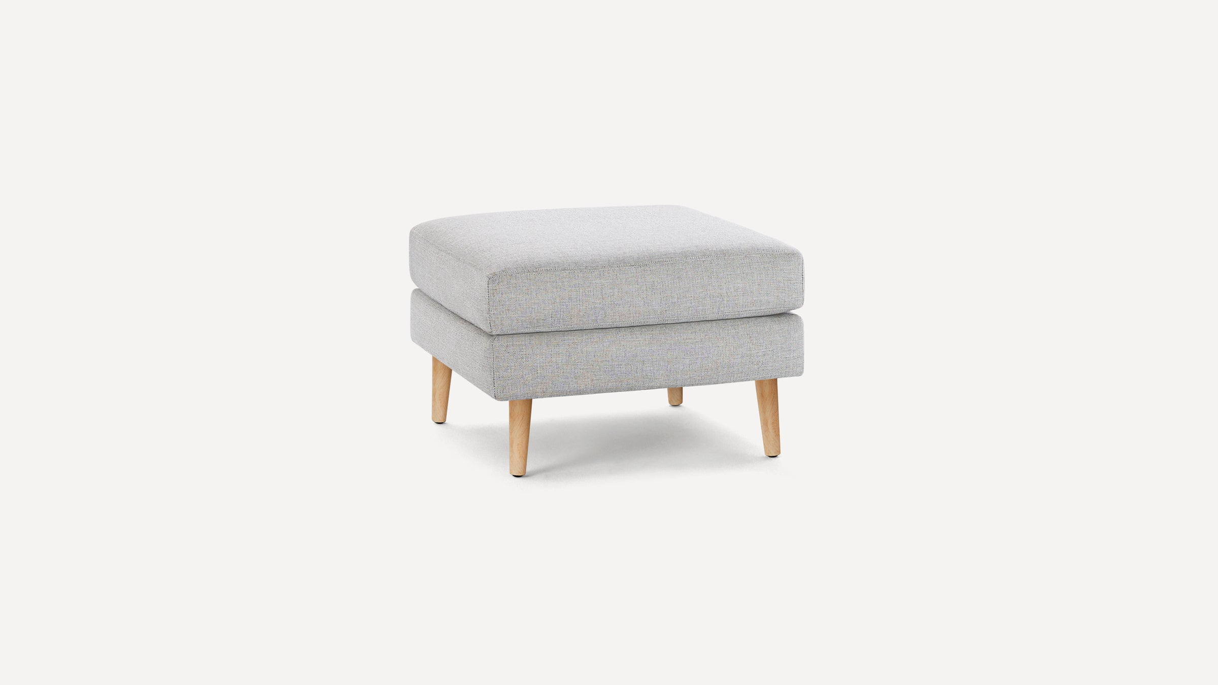 Light gray fabric ottoman with a thick cushion and four angled wooden legs on a white background.