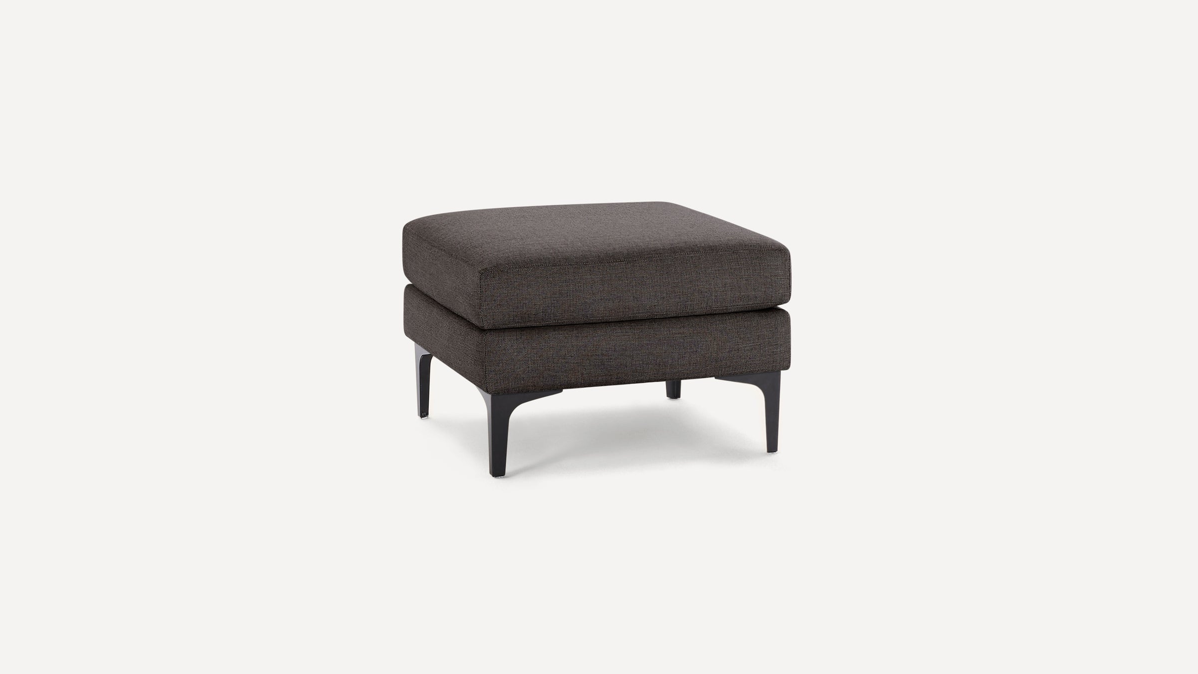 Square dark gray fabric ottoman with soft cushion top and black tapered legs on white background.