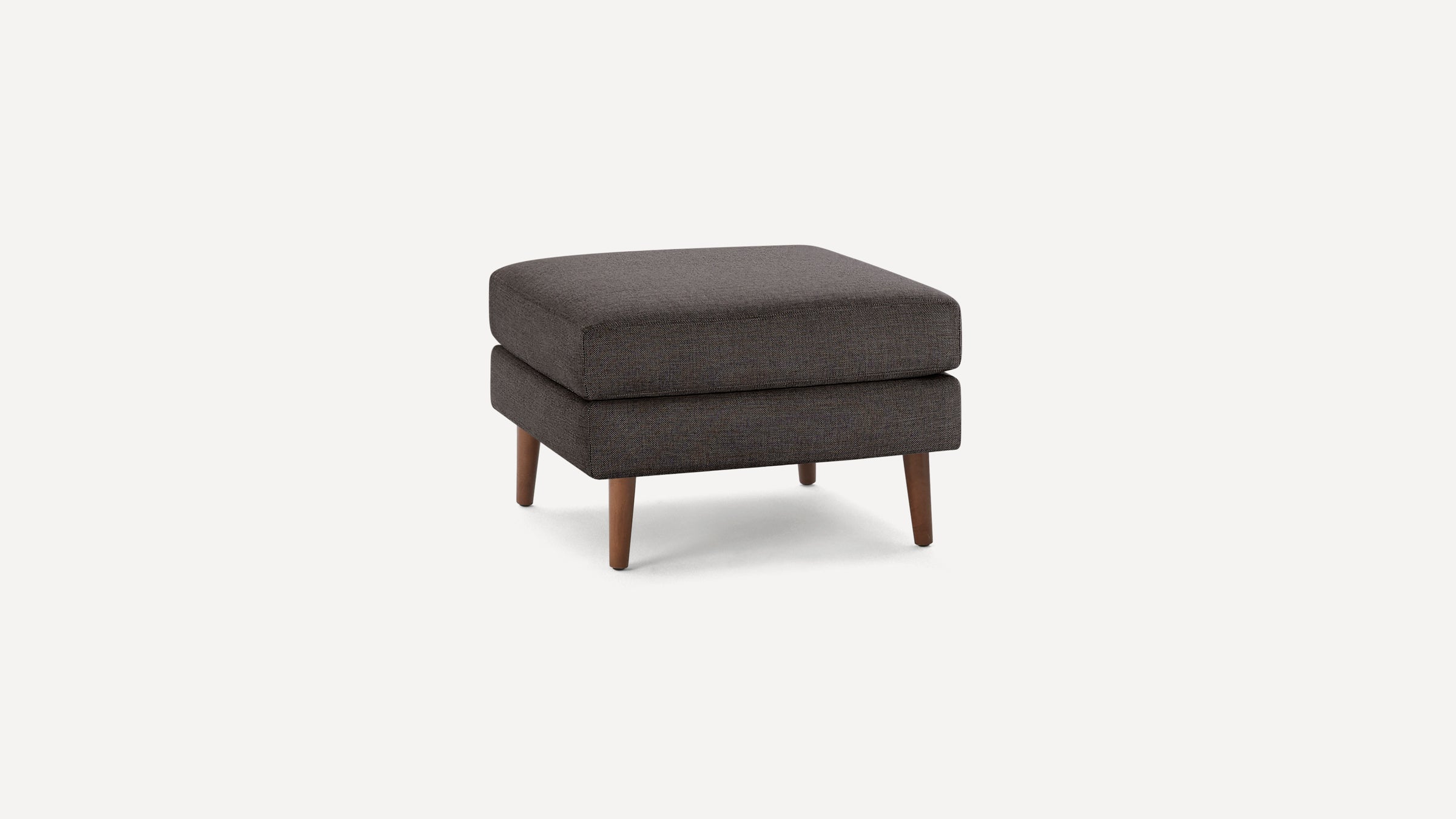 Square dark gray upholstered ottoman with wooden tapered legs on a plain white background.