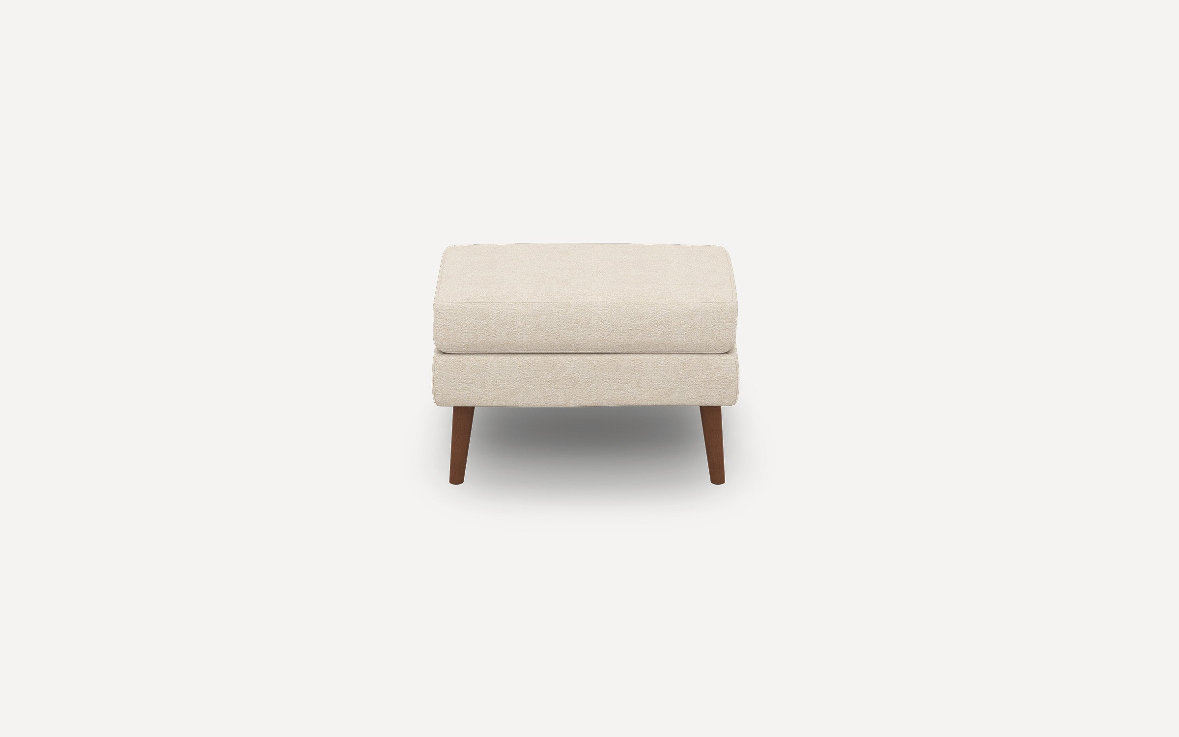 Beige upholstered rectangular ottoman with cushioned top and tapered wooden legs, shown on white background.