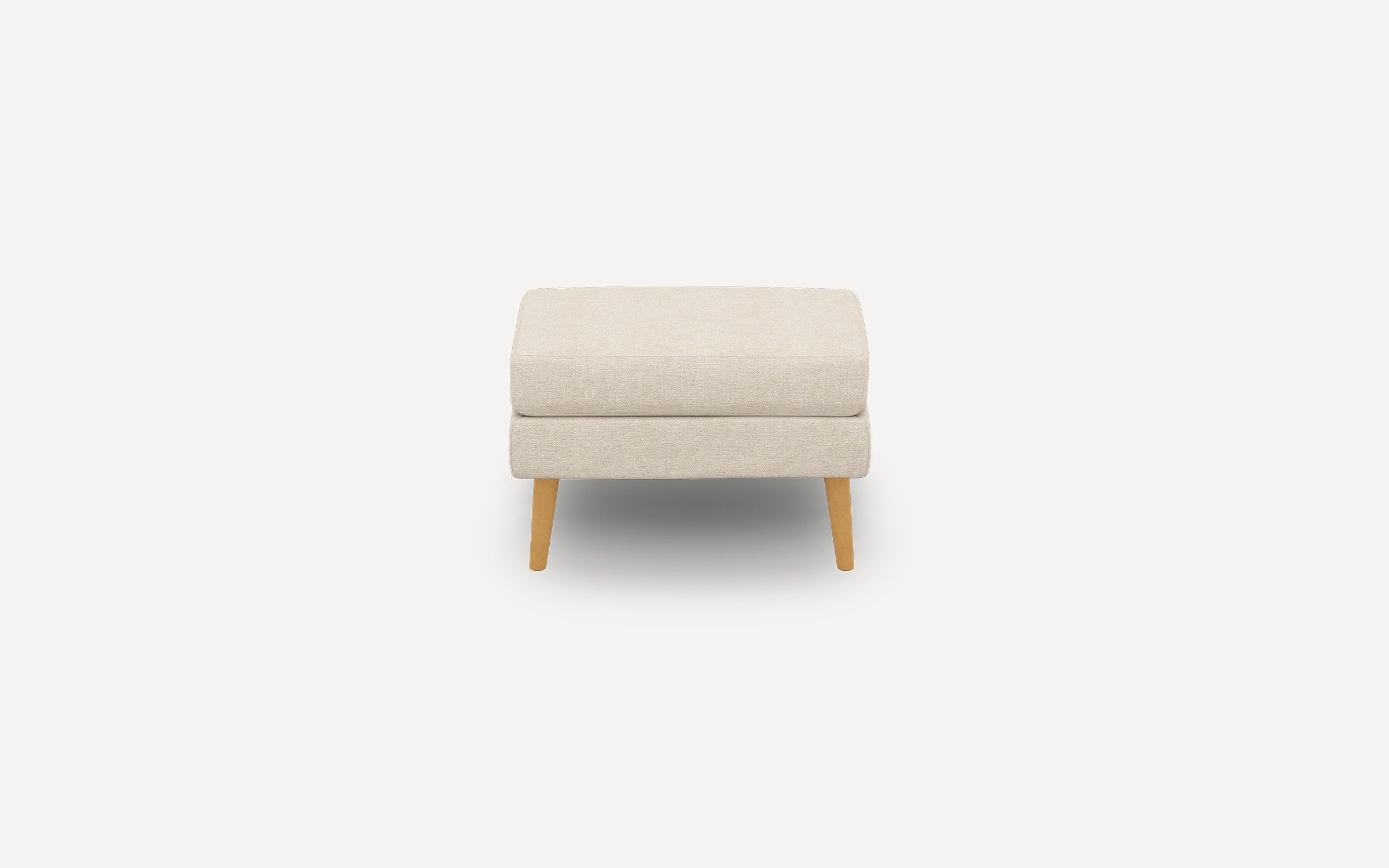 Beige fabric upholstered ottoman with two stacked cushions and four wooden legs, shown against a white background.
