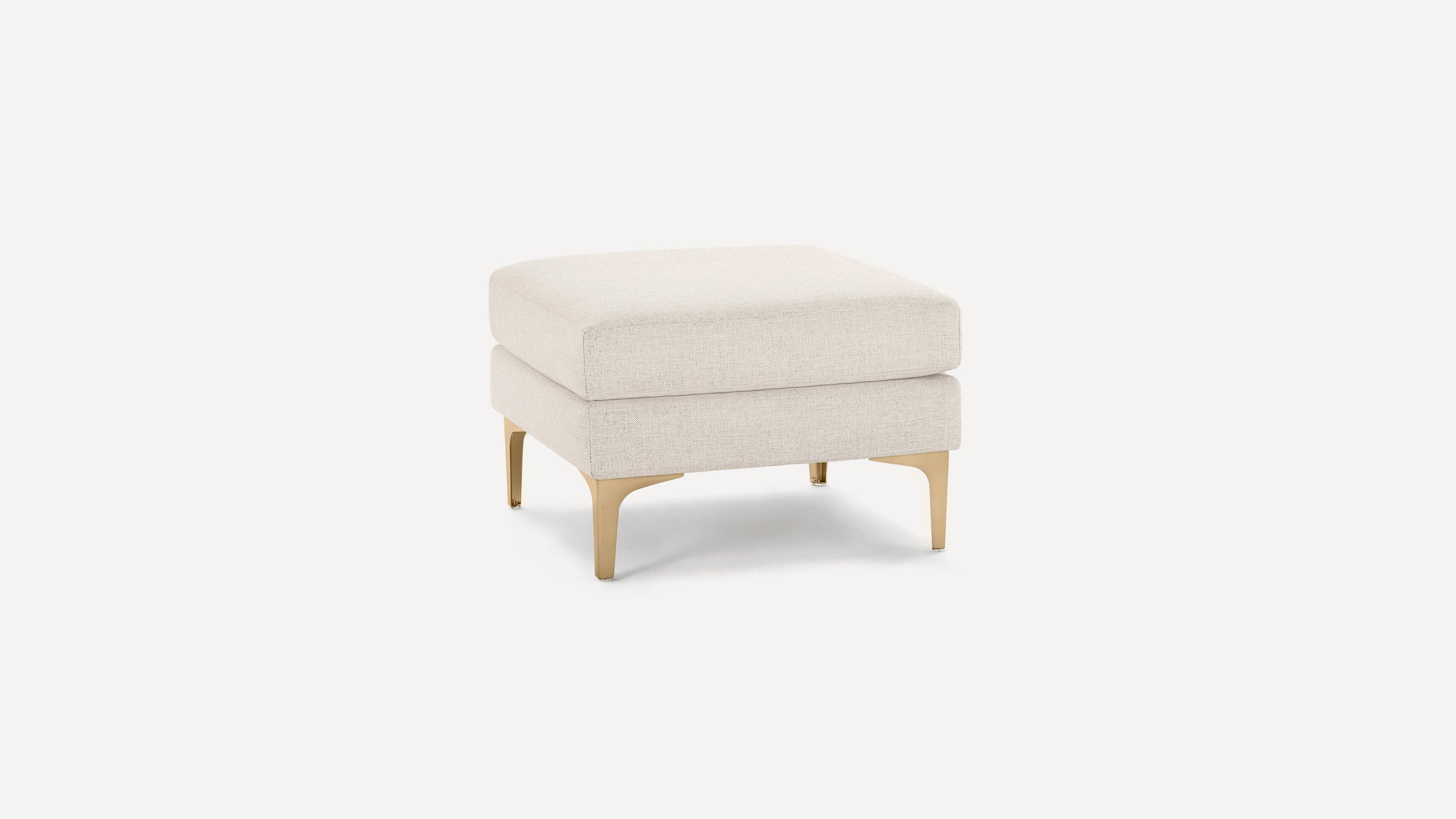 Square beige upholstered ottoman with padded cushion and four gold metal legs on a white background.