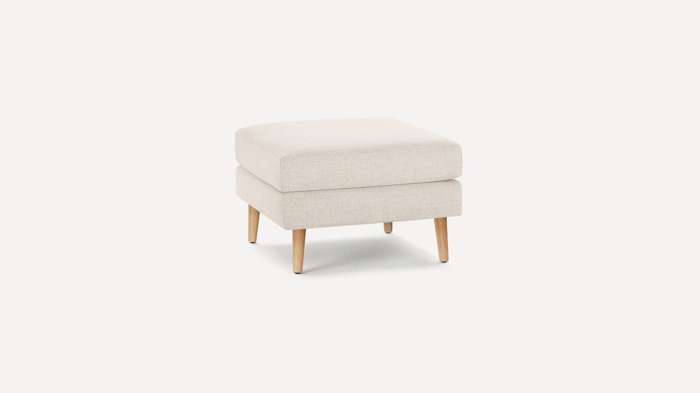 Beige fabric ottoman with a cushioned top and wooden tapered legs, shown against a plain white background.