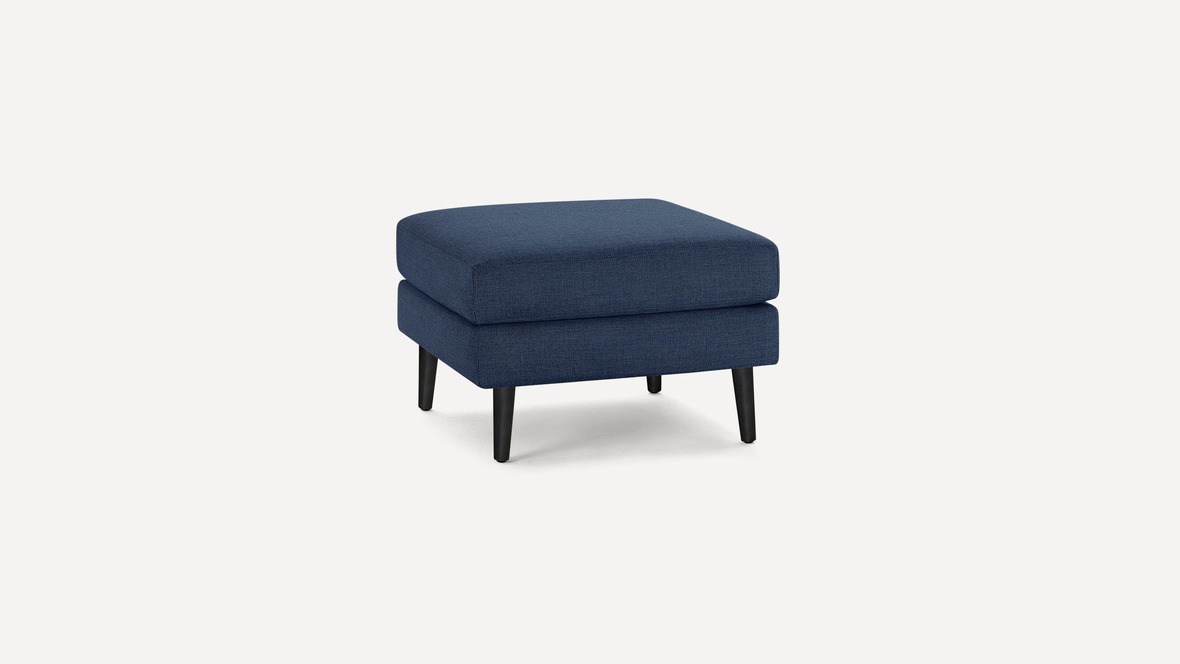 Square navy blue fabric ottoman with black tapered wooden legs on a plain white background.