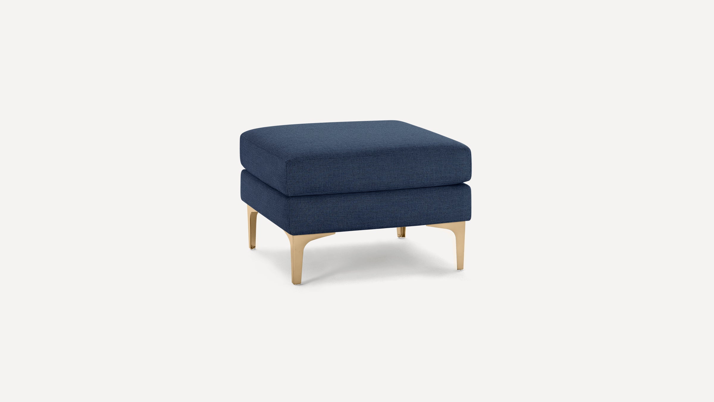 Square navy blue upholstered ottoman with gold metal legs on a white background.