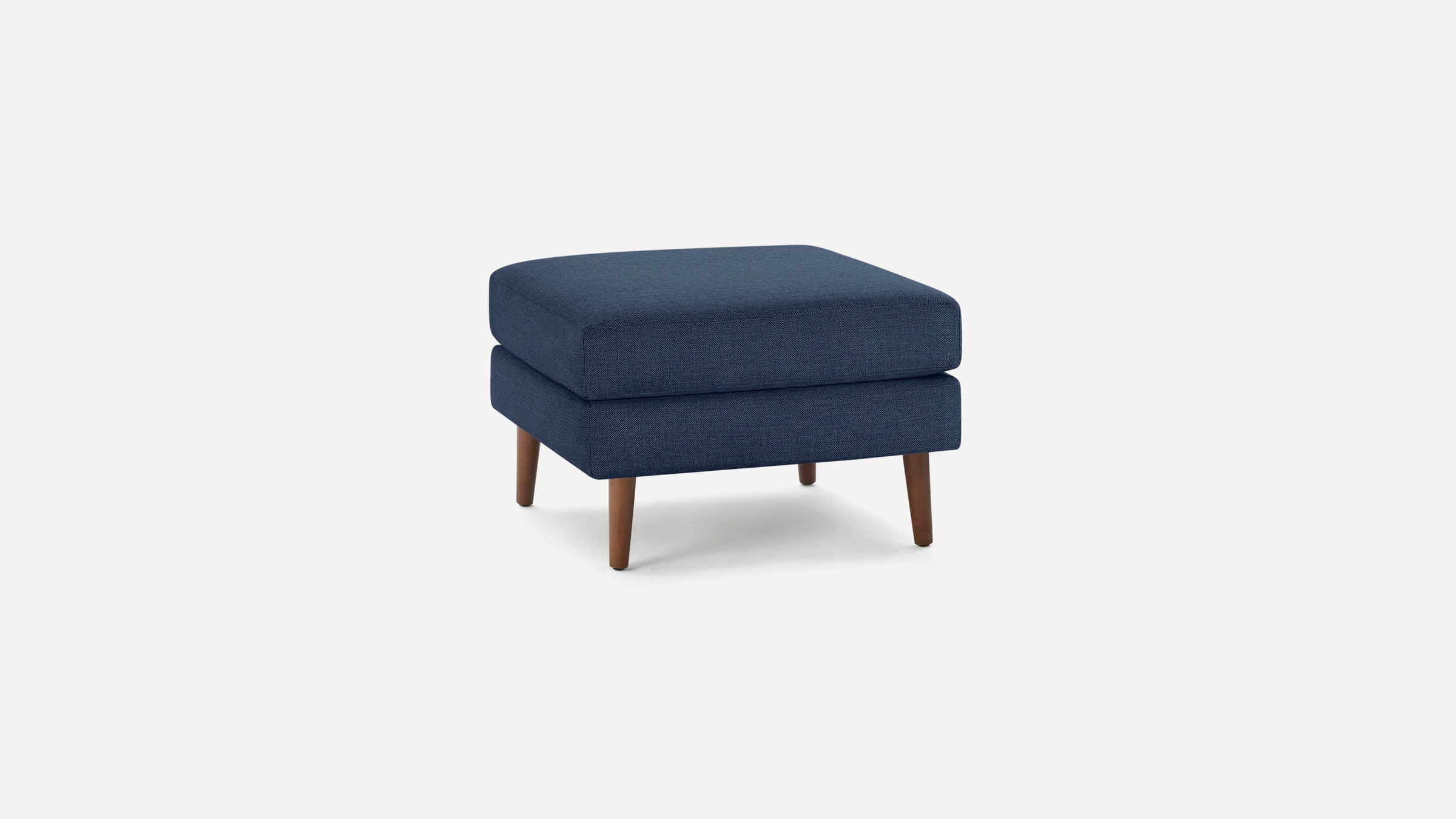 Square navy blue upholstered ottoman with wooden tapered legs on a white background.