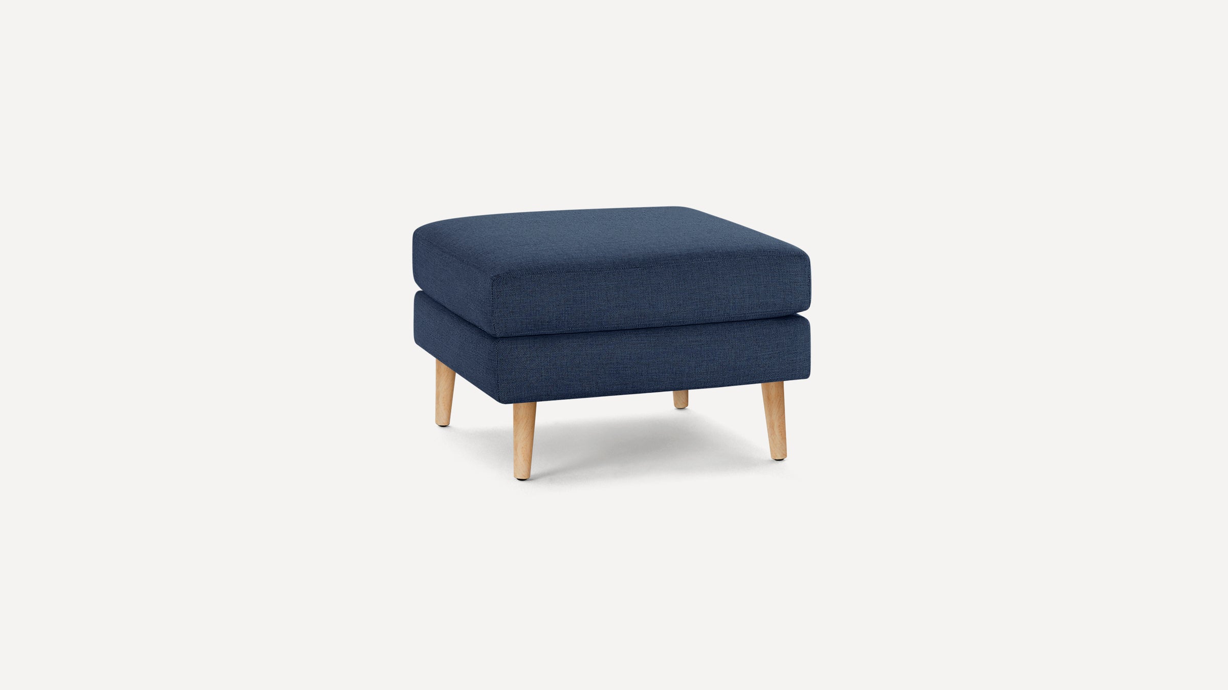 Square navy blue upholstered ottoman with light wooden tapered legs on a plain white background.