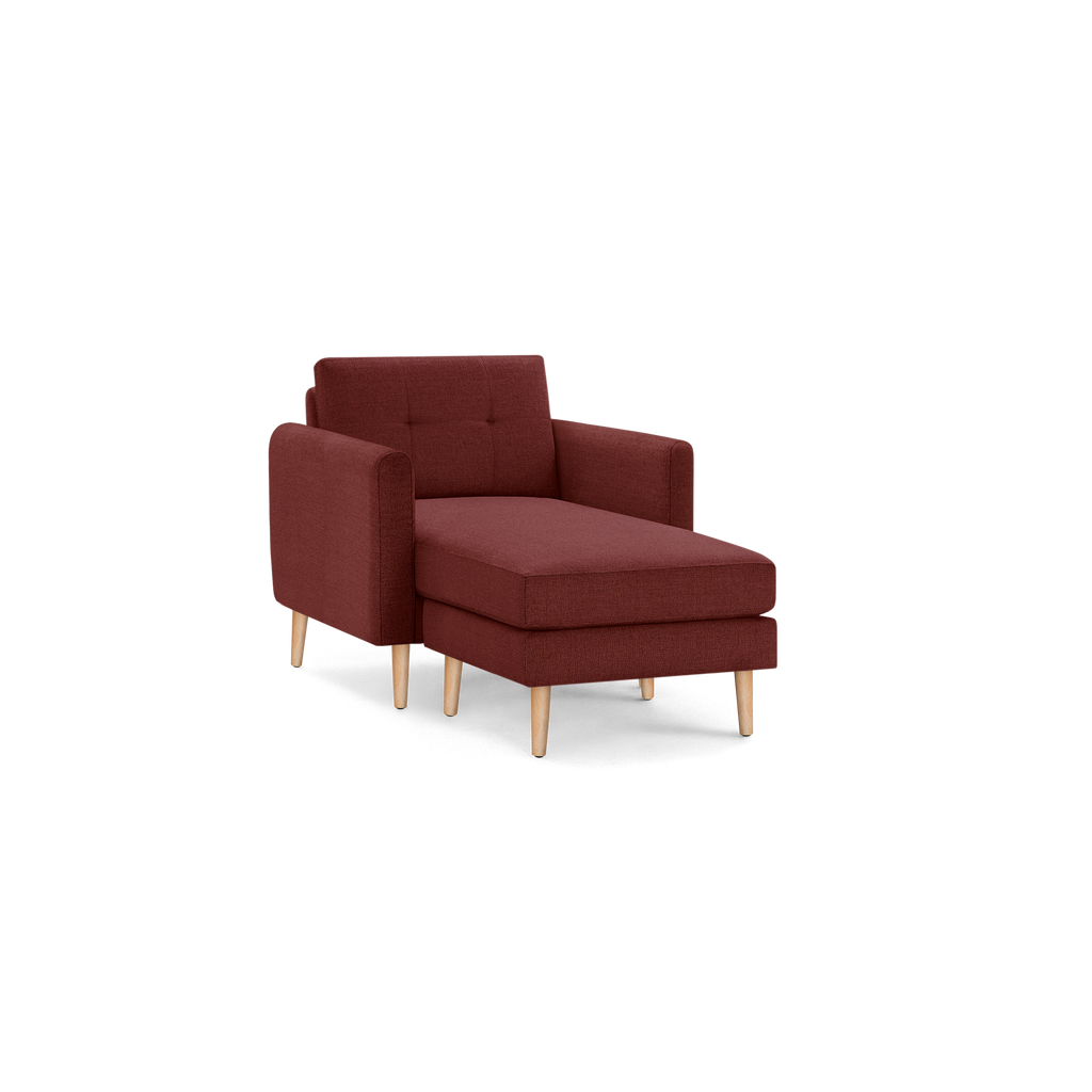 Modern chaise lounge chair with tufted backrest, upholstered in deep burgundy fabric, supported by light wooden legs.