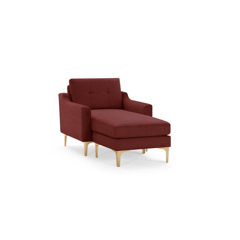 Modern burgundy upholstered chaise lounge chair with a tufted backrest and gold metal legs on a black background.