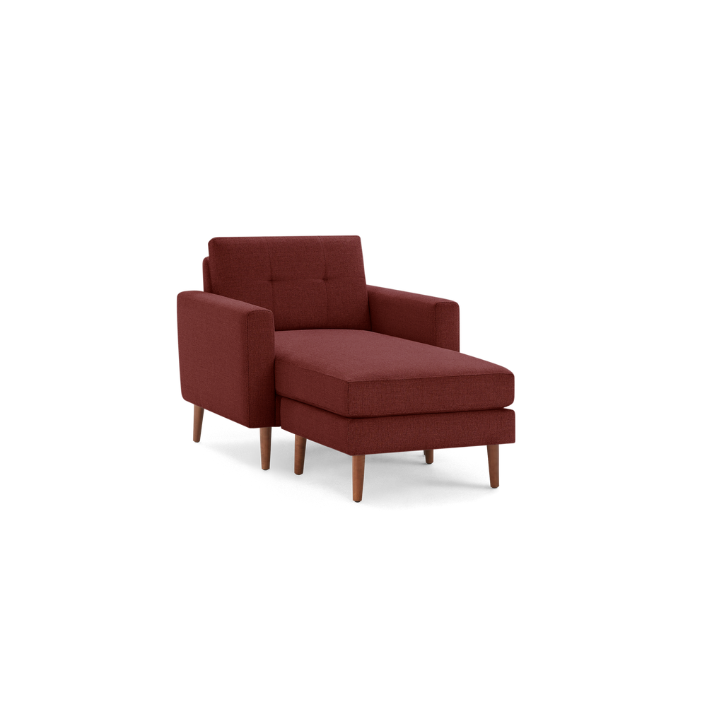 Modern deep red upholstered chaise lounge chair with wooden legs and tufted backrest, isolated on black background.