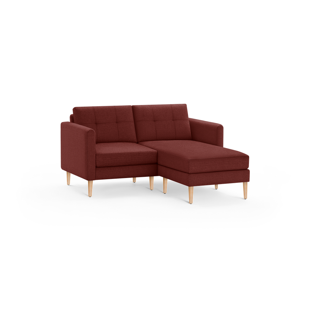 Modern sectional sofa with chaise lounge, upholstered in dark red fabric, featuring tufted back cushions and light wooden legs.