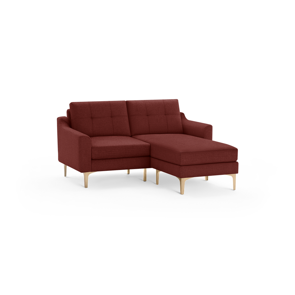Modern deep red upholstered sectional sofa with tufted back cushions and light wooden legs, featuring a chaise lounge on the right side.
