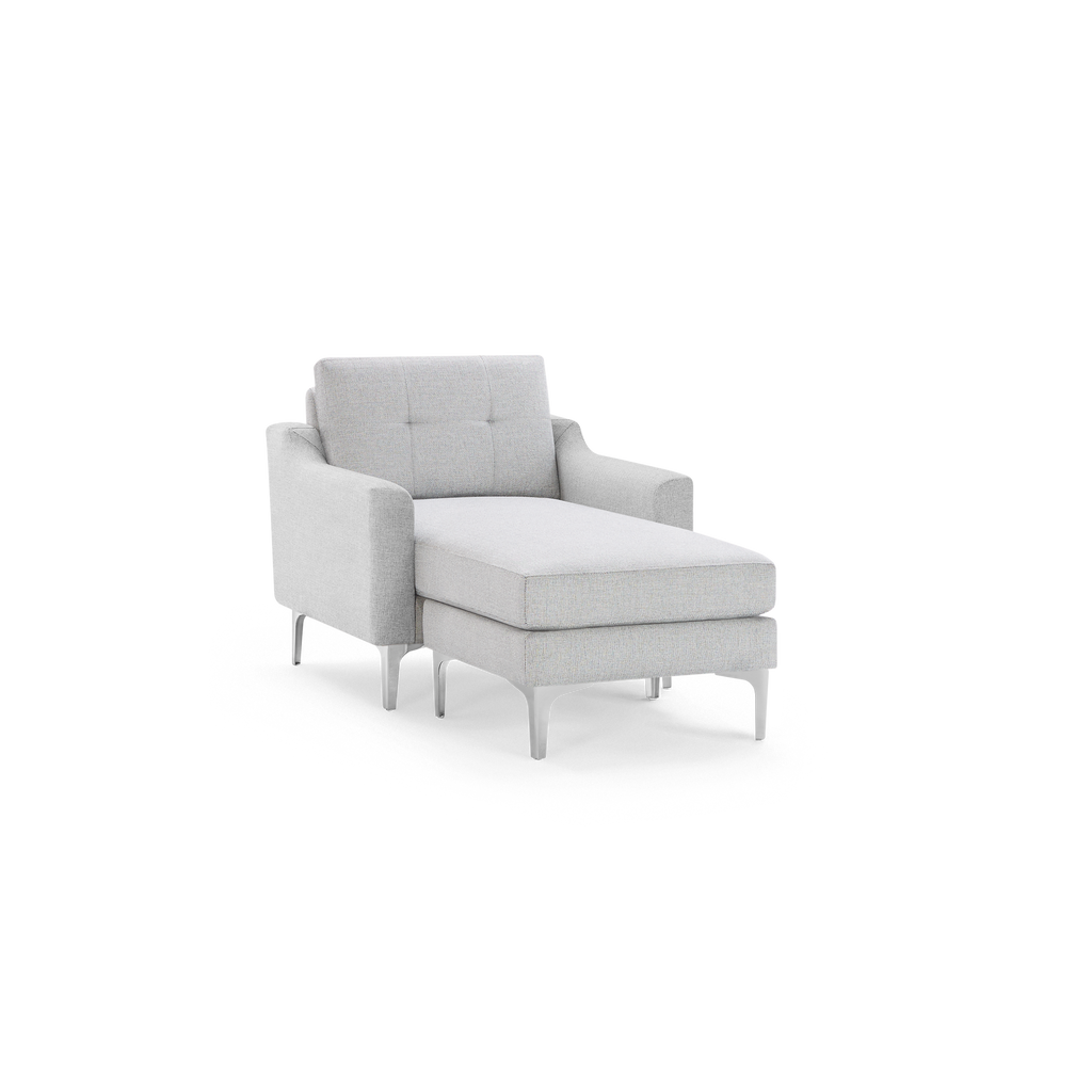 Light gray upholstered chaise lounge chair with tufted backrest, angled armrests, and slim metal legs, isolated on black background.