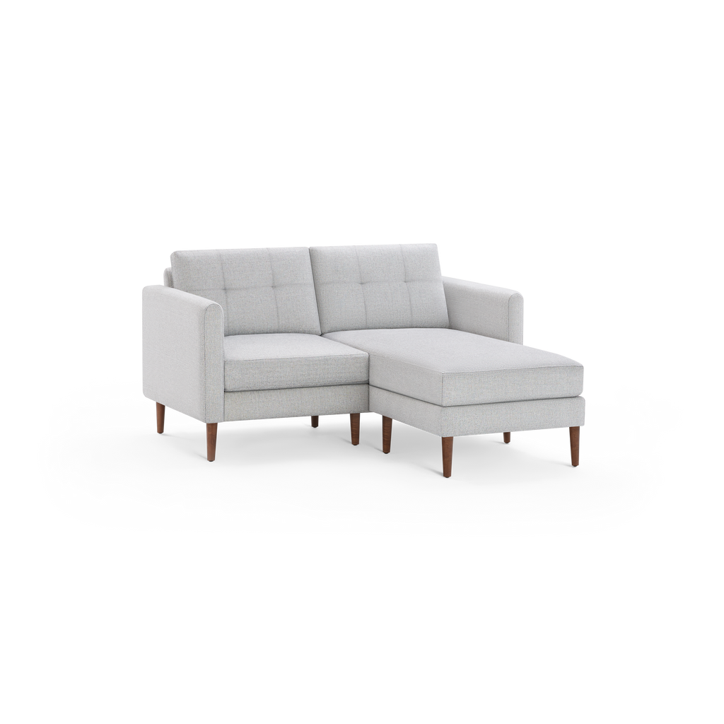 Light gray upholstered sectional sofa with tufted back cushions and wooden legs, featuring a chaise lounge on the right side.