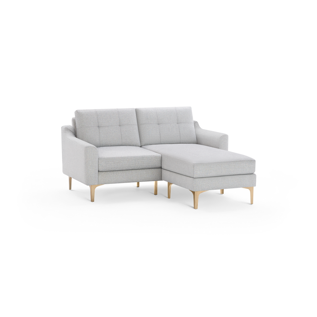 Light gray fabric sectional sofa with tufted back cushions and wooden legs, featuring a chaise lounge on the right side.