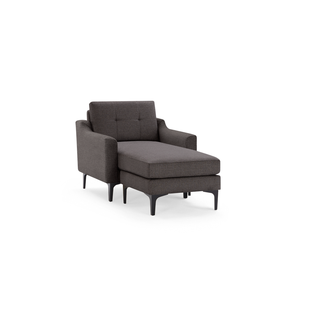 Dark gray upholstered armchair with extended chaise lounge, tufted backrest, and black slim legs, isolated on black background.