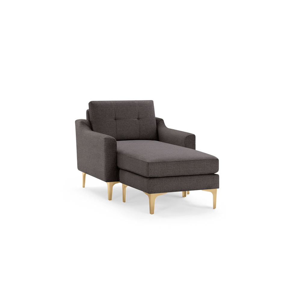 Modern dark gray fabric chaise lounge chair with tufted backrest, armrests, and gold-toned metal legs on black background.
