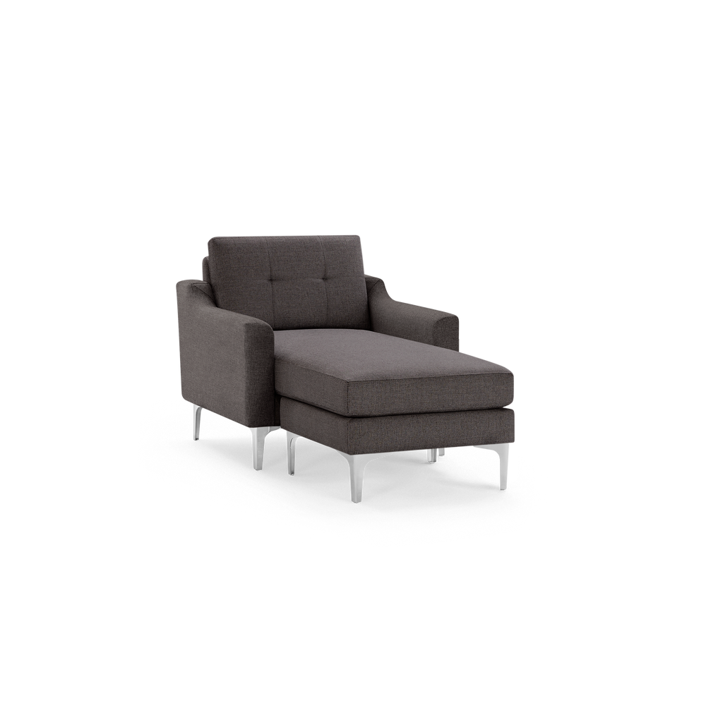 Modern dark gray fabric chaise lounge chair with tufted backrest and sleek silver metal legs, isolated on black background.