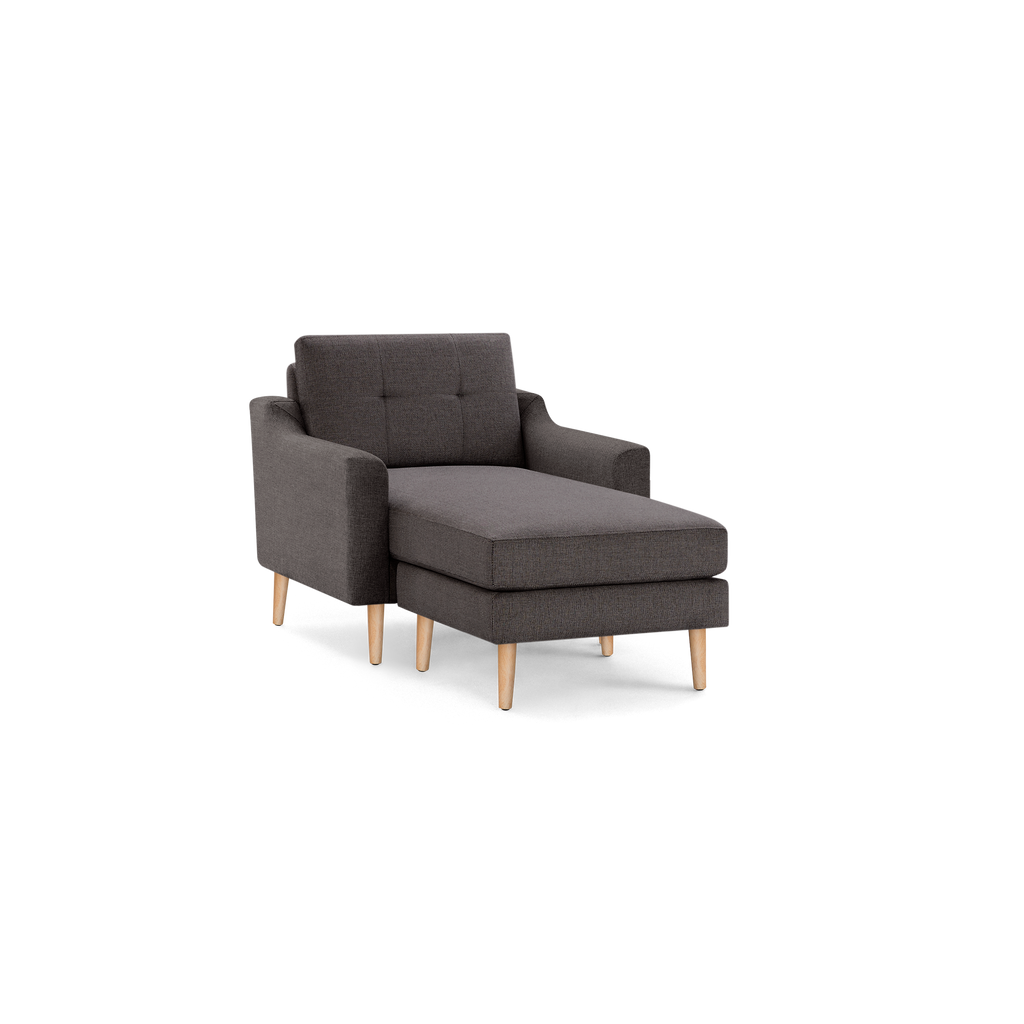 Dark gray upholstered chaise lounge chair with tufted backrest and light wooden legs, isolated on black background.