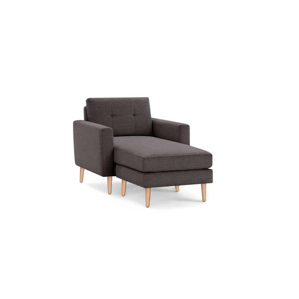 Dark gray fabric chaise lounge chair with button-tufted backrest and light wooden legs, modern and compact design.