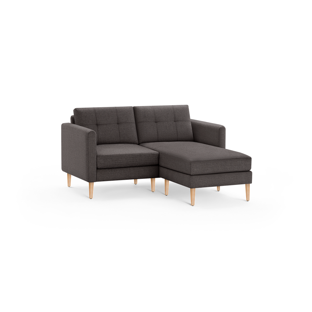 Dark gray fabric sectional sofa with tufted cushions, wooden legs, and chaise lounge on right side, modern design.