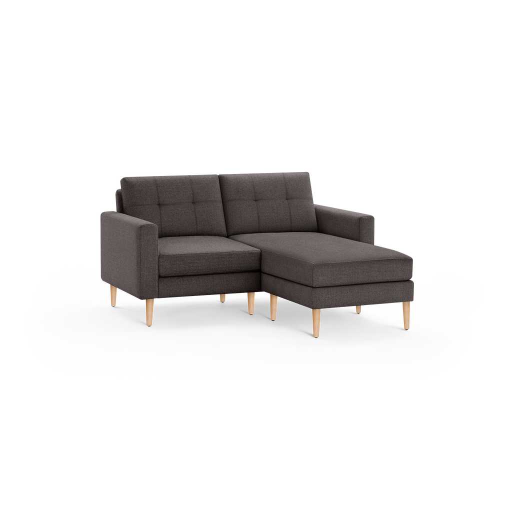 Dark gray fabric sectional sofa with tufted back cushions and light wooden legs, featuring a chaise lounge on the right side.