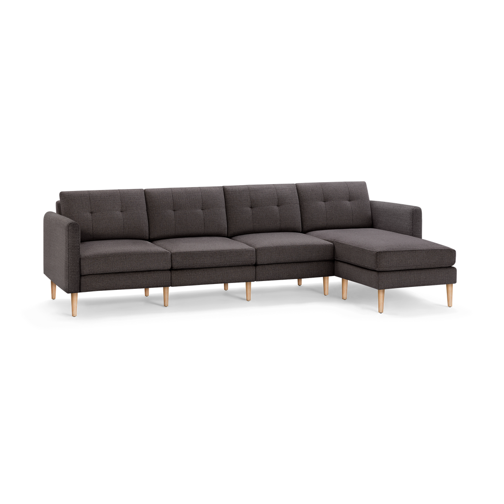 Dark gray fabric sectional sofa with tufted back cushions and light wooden legs, featuring a chaise lounge on the right side.
