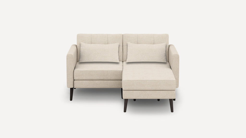 Beige two-seater sectional sofa with chaise lounge, cushioned seats, backrests, armrests, and two matching rectangular pillows.