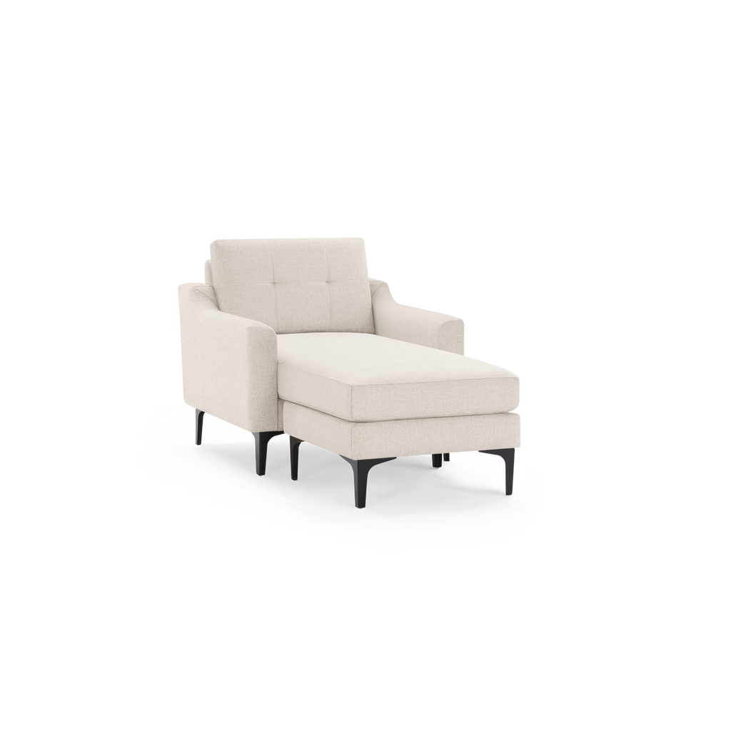 Beige upholstered chaise lounge chair with tufted backrest and black tapered legs on a black background.