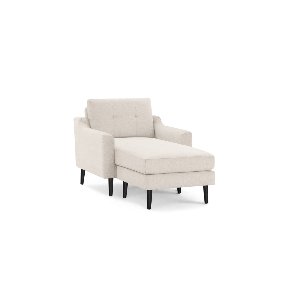Beige upholstered chaise lounge chair with tufted backrest, padded armrests, and tapered dark wooden legs.
