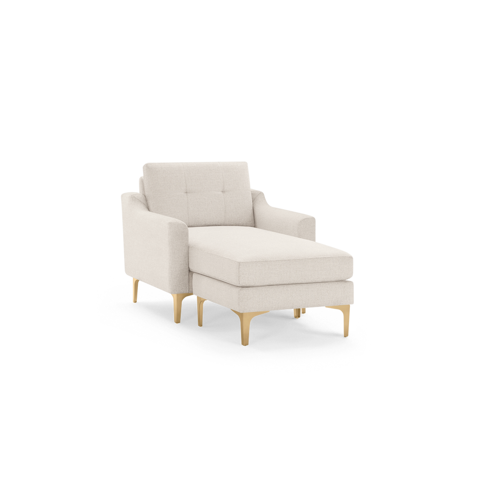 Beige upholstered chaise lounge chair with tufted backrest and sleek light wooden legs on black background.