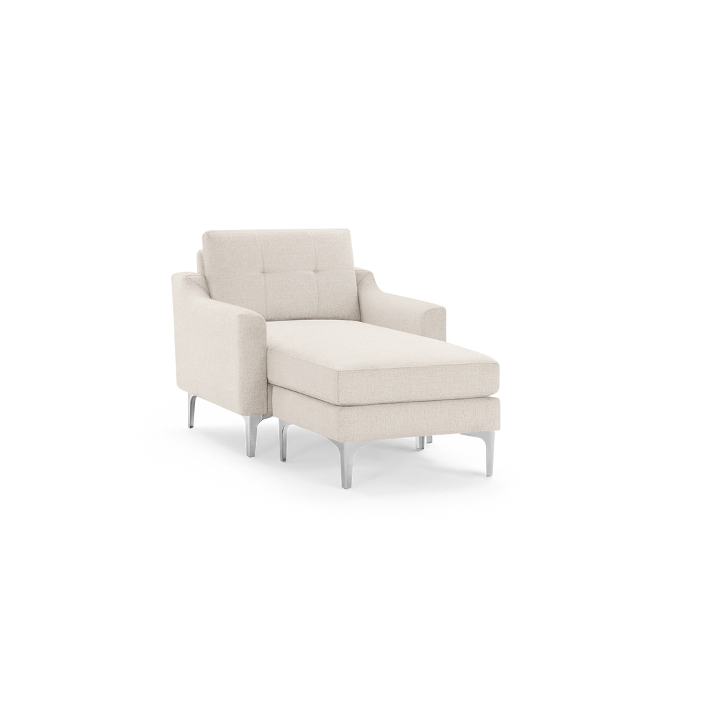Beige fabric chaise lounge chair with tufted backrest, padded armrests, and sleek silver metal legs on black background.