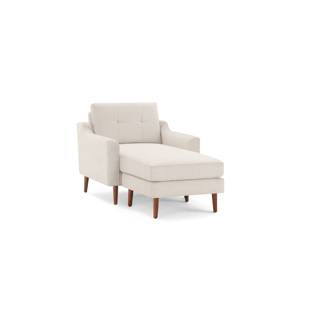 Beige upholstered chaise lounge with mid-century tufted backrest and brown wooden legs on black background.