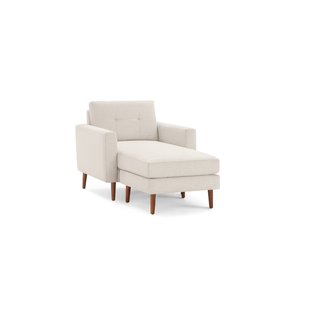 Beige fabric chaise lounge chair with square tufted backrest, cushioned seat, armrests, and wooden tapered legs.