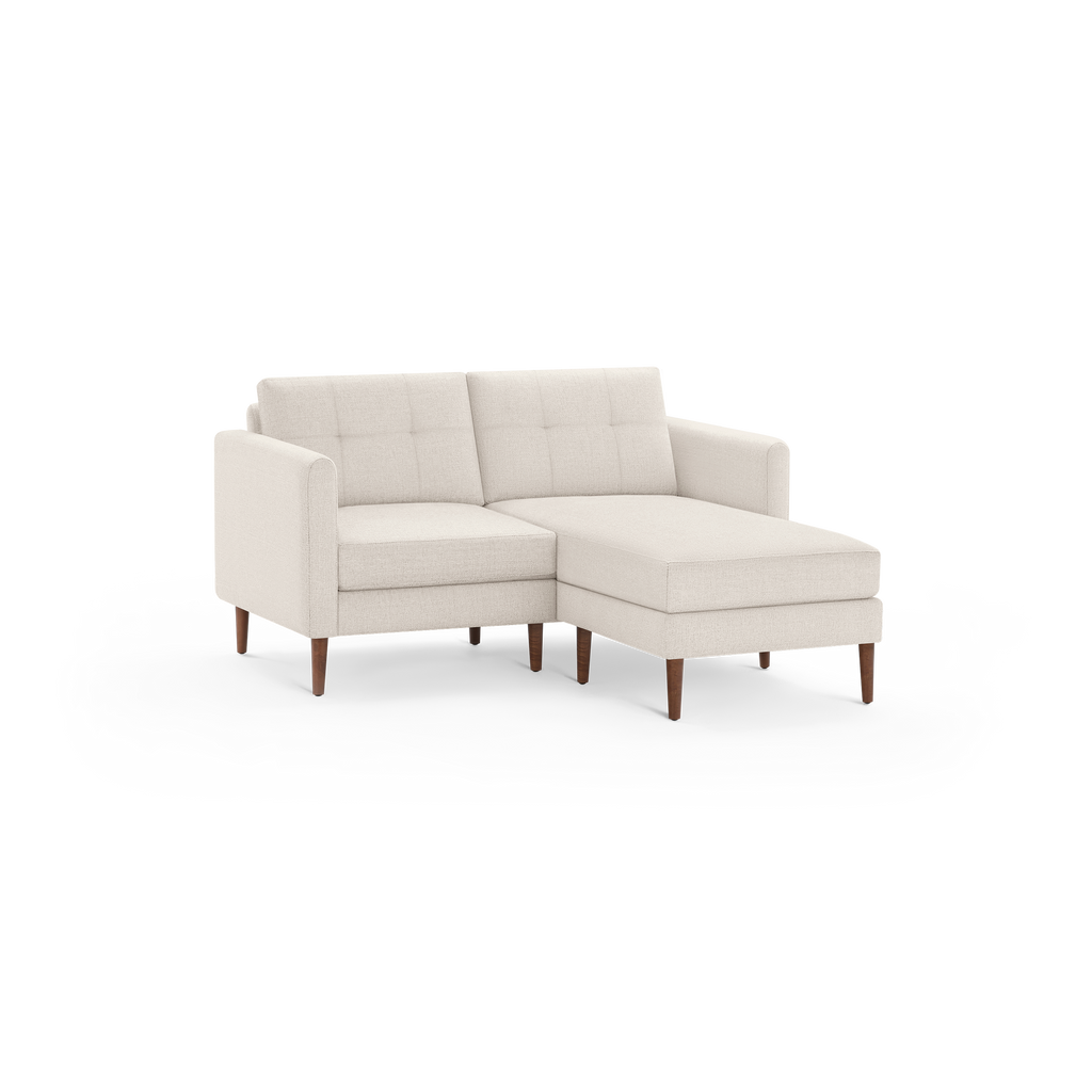 Beige fabric sectional sofa with tufted back cushions, wooden tapered legs, and a chaise lounge on the right side.