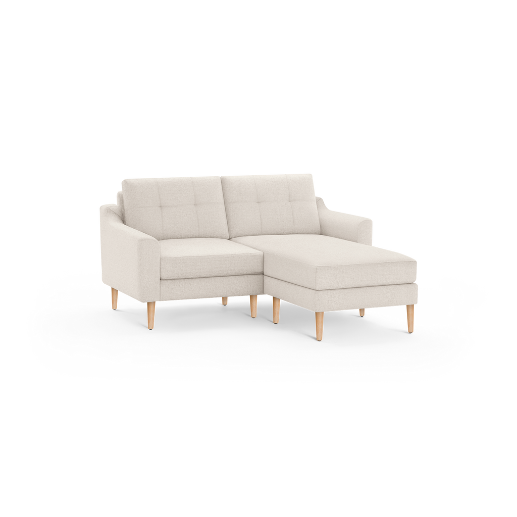 Beige fabric sectional sofa with tufted back cushions, wooden legs, and a chaise lounge on the right side.