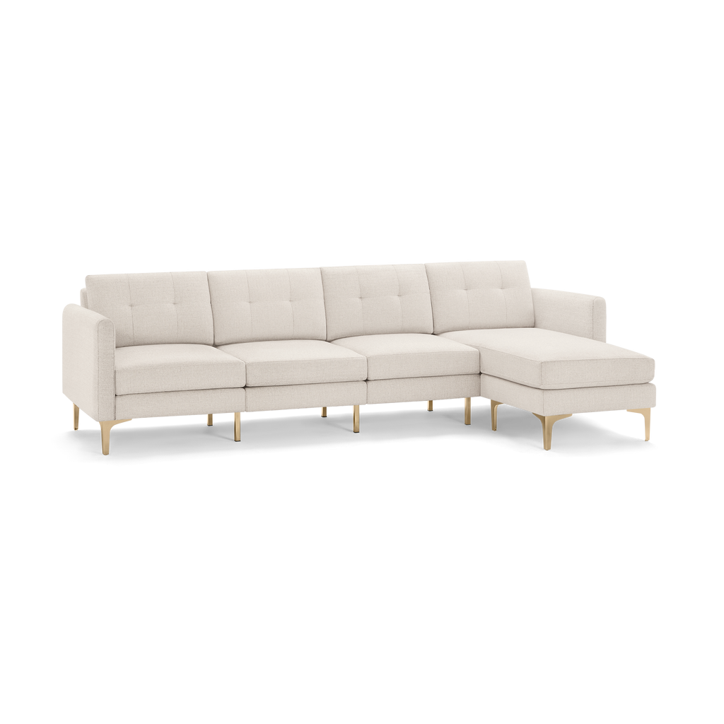 Light beige fabric sectional sofa with tufted back cushions, gold metallic legs, and an attached chaise lounge on the right side.