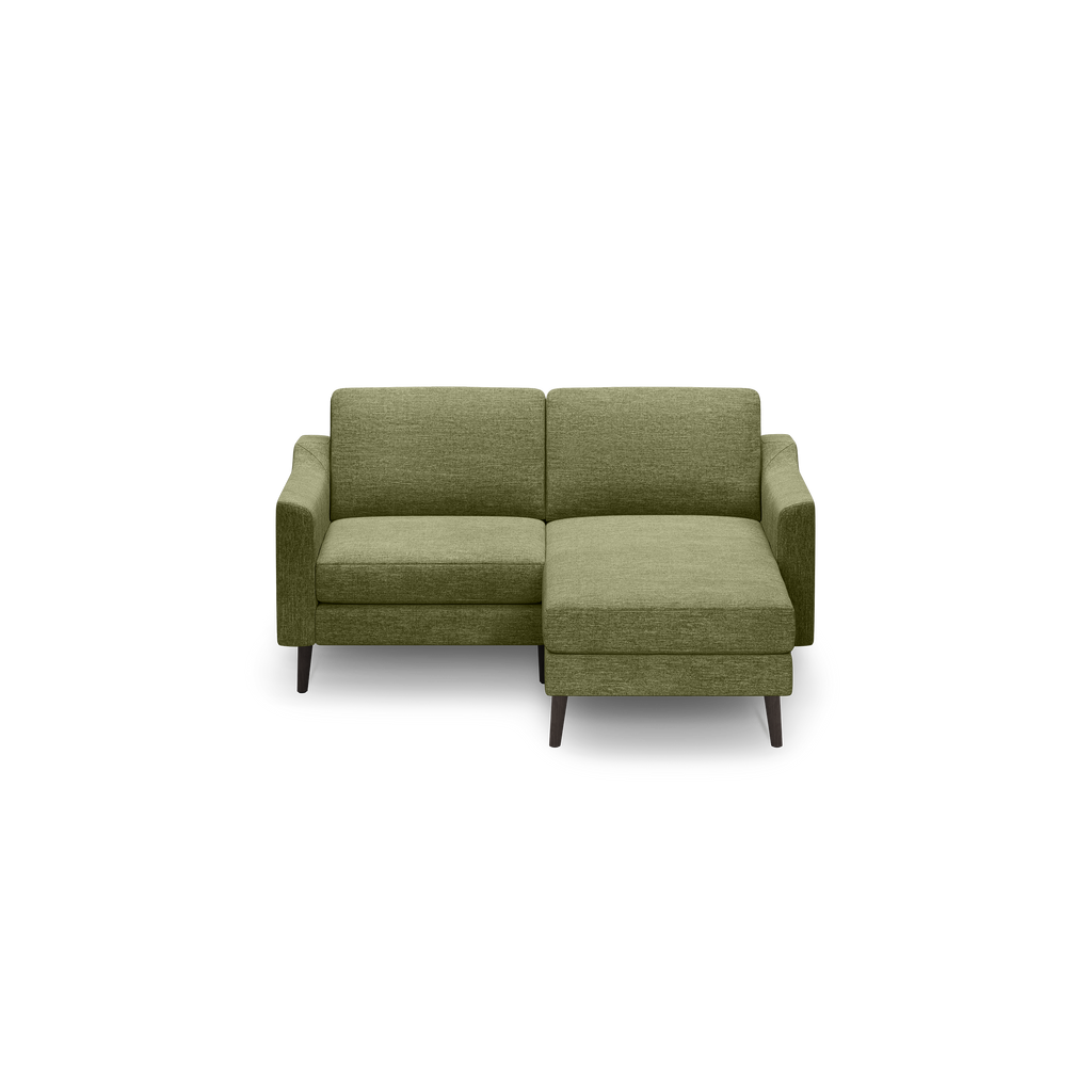 Green upholstered modern sectional sofa with chaise lounge and dark wooden legs against a black background.