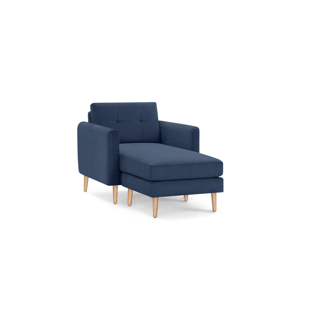 Modern navy blue chaise lounge chair with tufted backrest and light wooden tapered legs, isolated on black background.