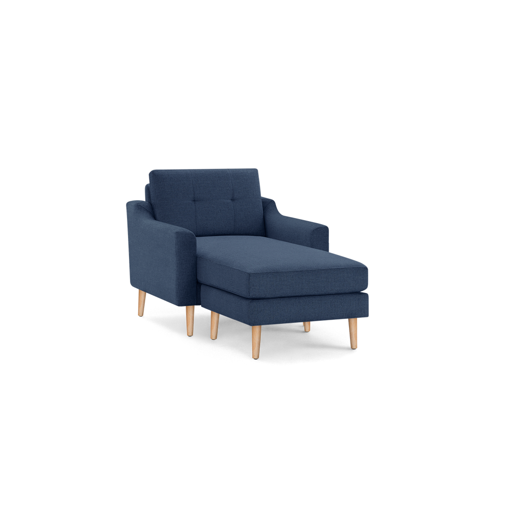 Blue upholstered chaise lounge chair with wooden legs, cushioned seat, tufted backrest, and armrests, isolated on black background.