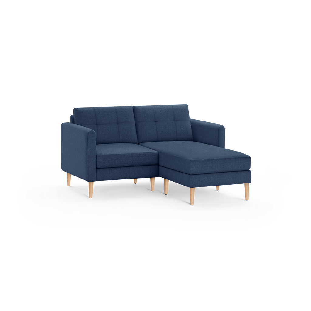 Modern navy blue sectional sofa with tufted back cushions, wooden tapered legs, and a chaise lounge on the right side.