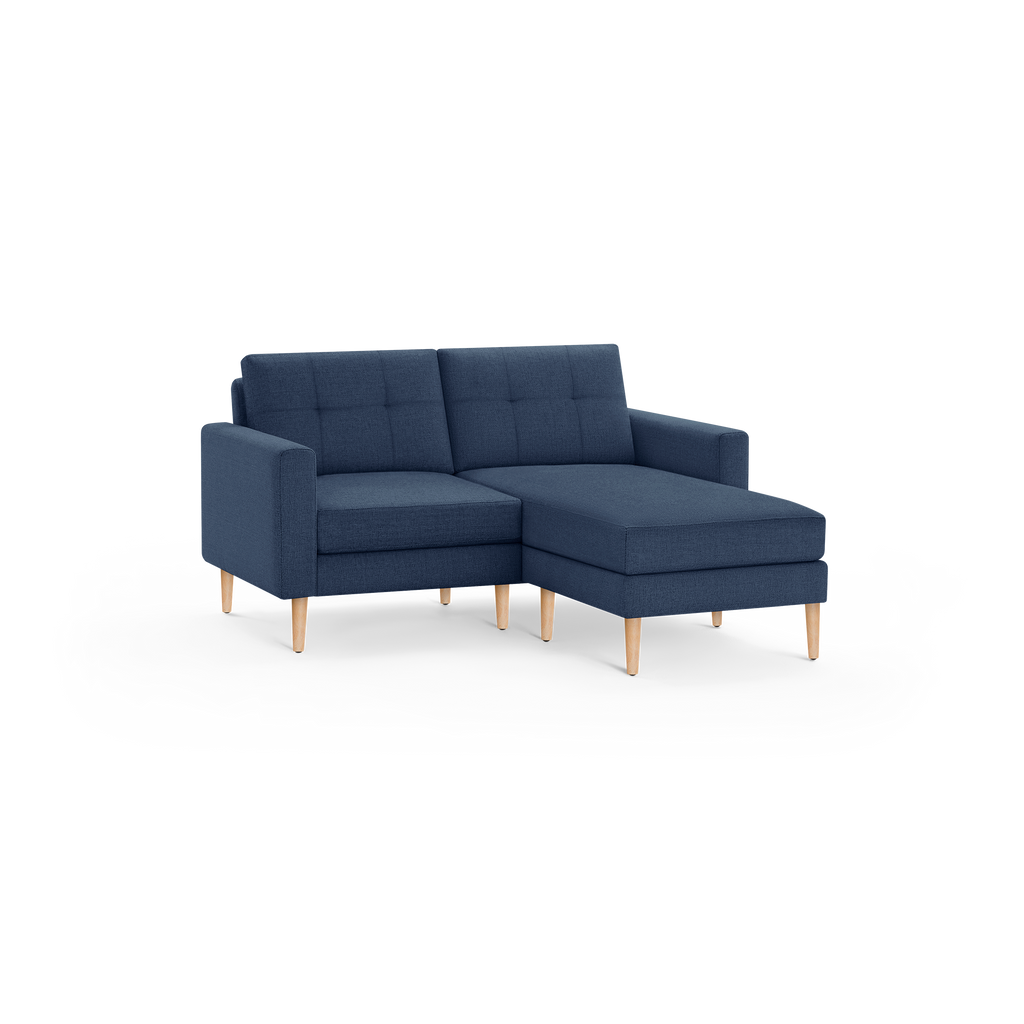 Mid-century modern navy blue sectional sofa with wooden legs and tufted back cushions, featuring a chaise lounge on the right side.