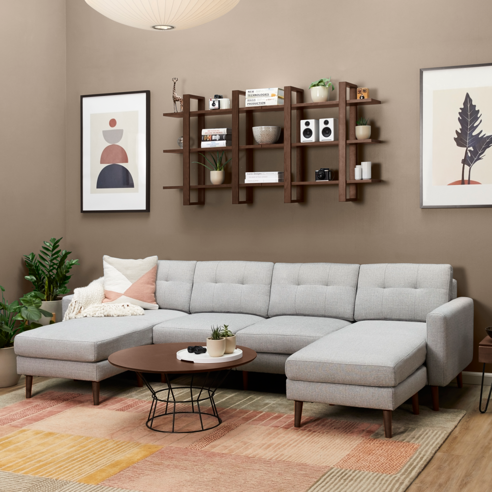 Light gray fabric sectional sofa with tufted cushions, wooden legs, and a modern round coffee table in a cozy living room setting.